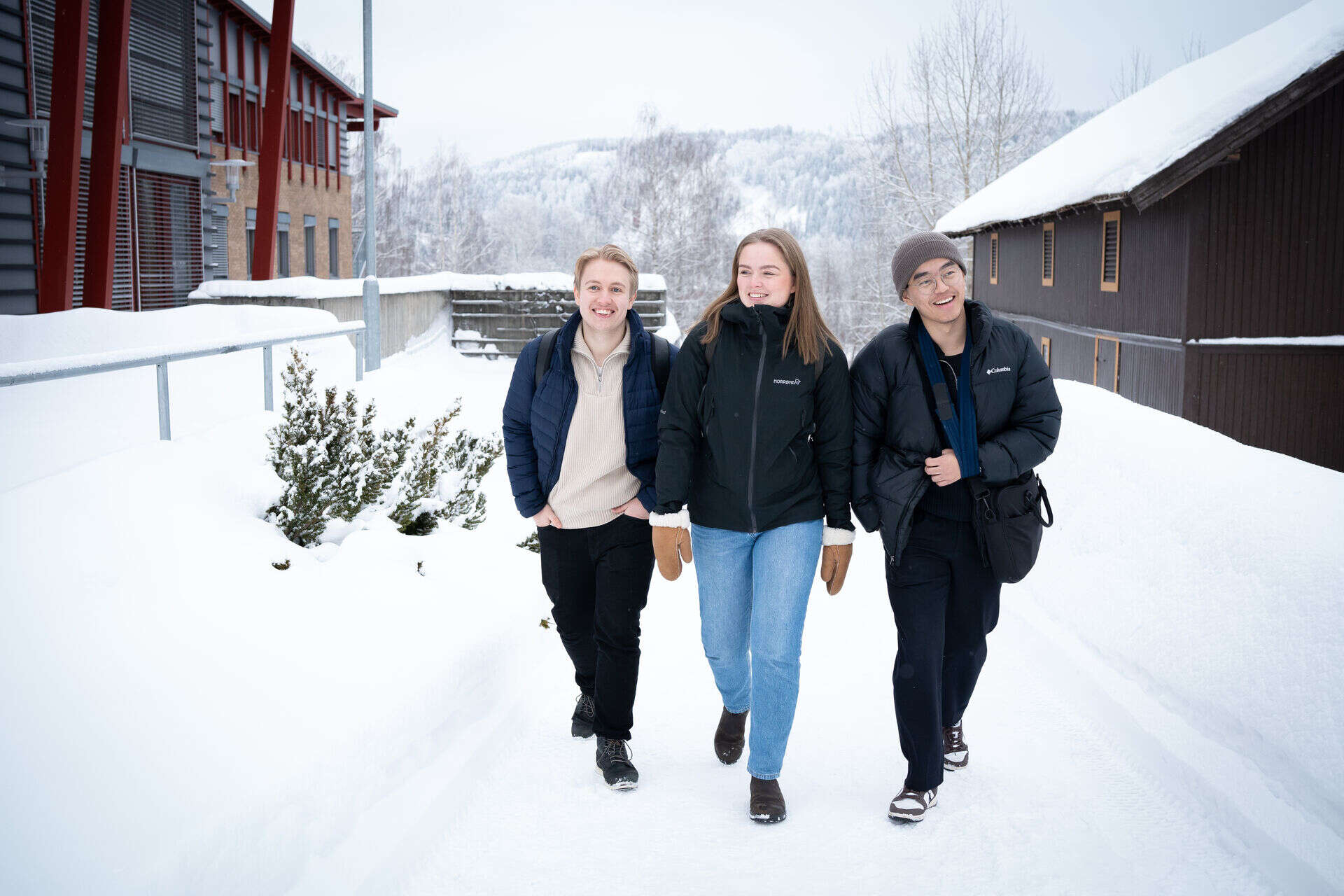 To gutter og en jente går med vinterklær utenfor universitetet på Rena. De smiler og er glade. Snøen har lagt seg og det ser litt kaldt ut.
