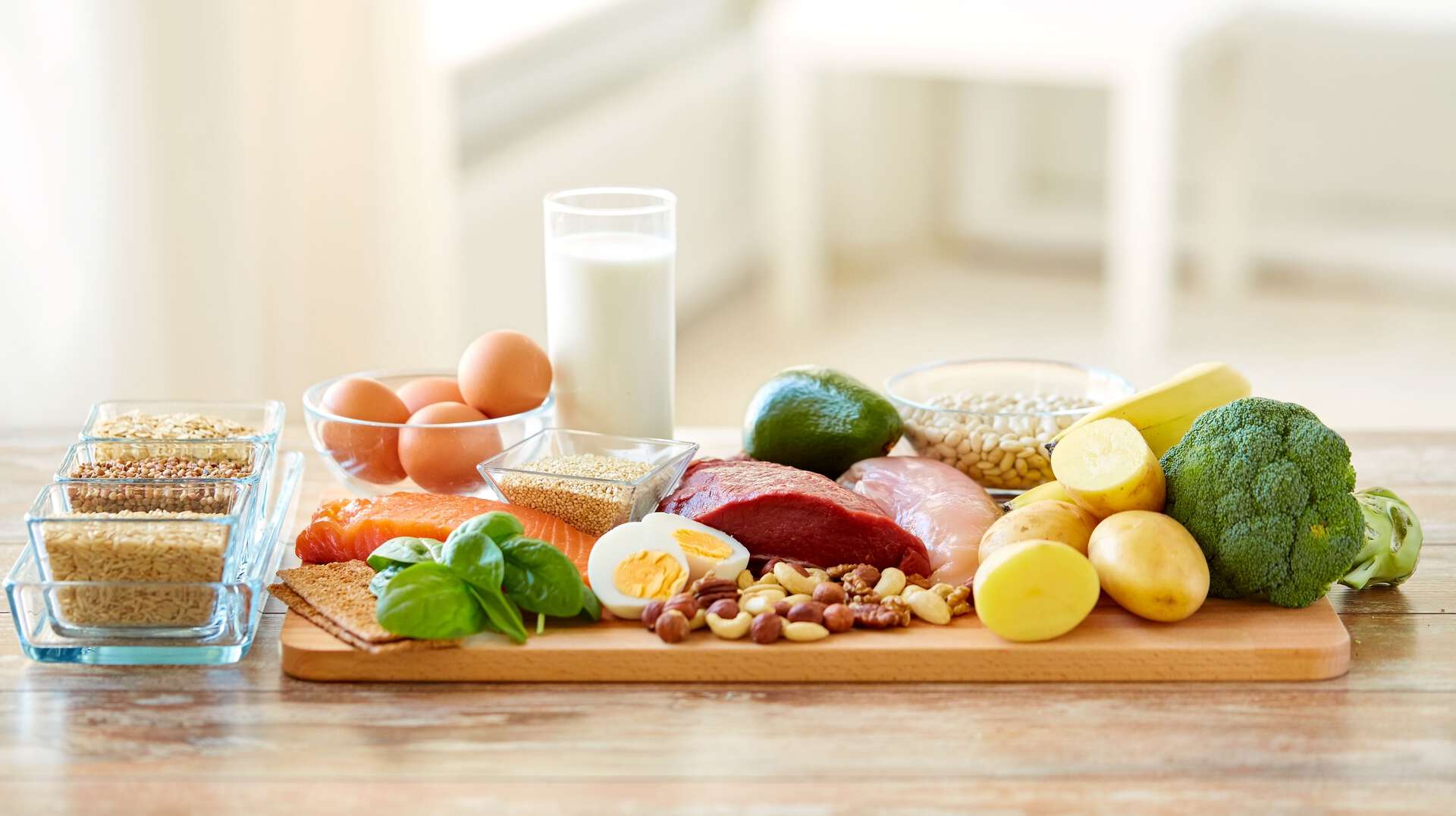 Et skjærebrett fult med mat, laks, egg, nøtter, potet, broccoli, nøtkjøtt. En skål med egg og et glass melk. Noe ris og gryn i små skåler ved siden av.