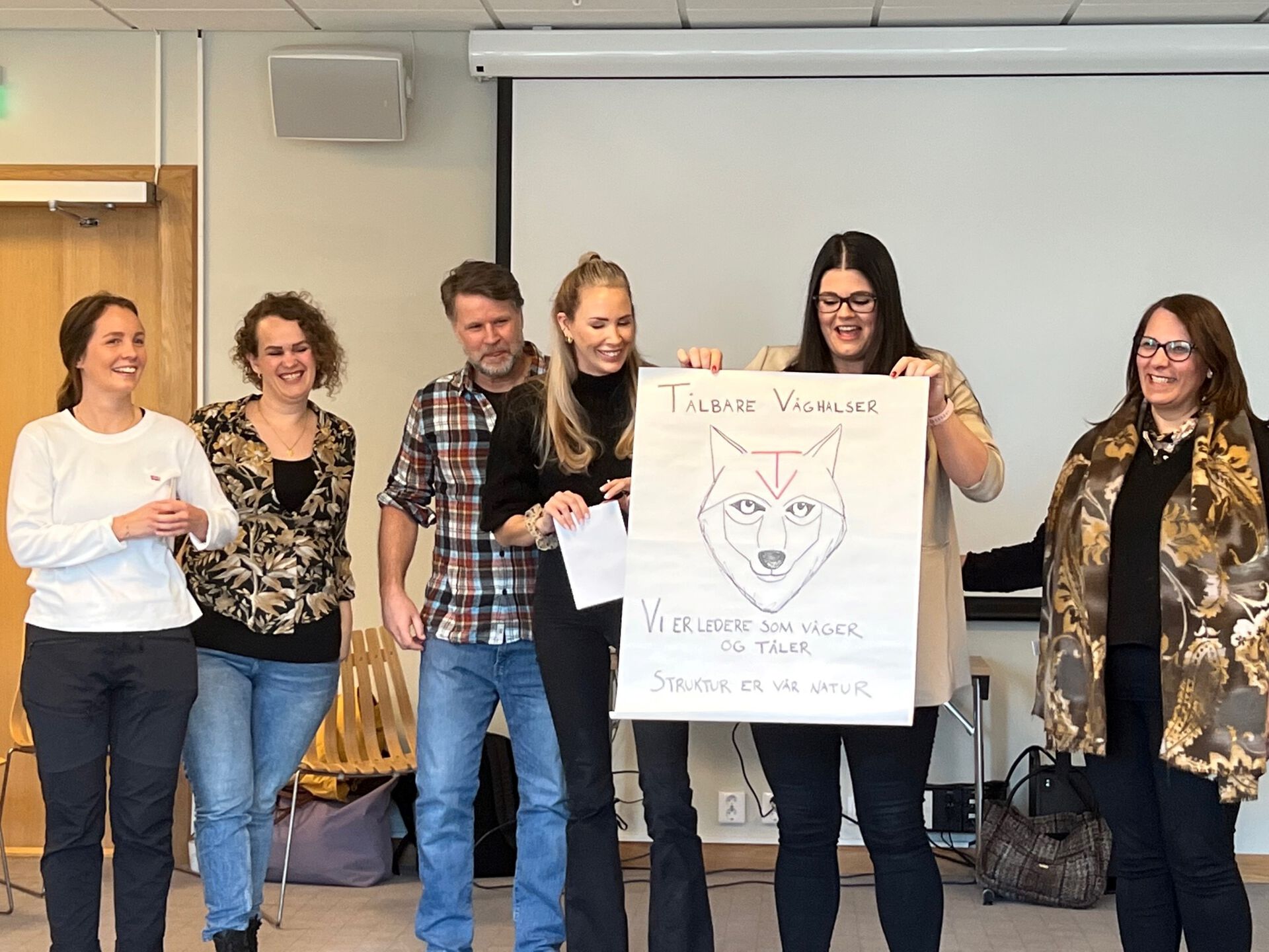 Seks studenter som viser frem en plakat med en tegnet ulv på. De smiler. 