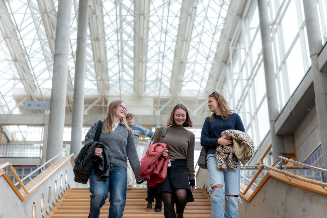 Studenter som går nedover en tretrapp. Lyst og åpent tak.