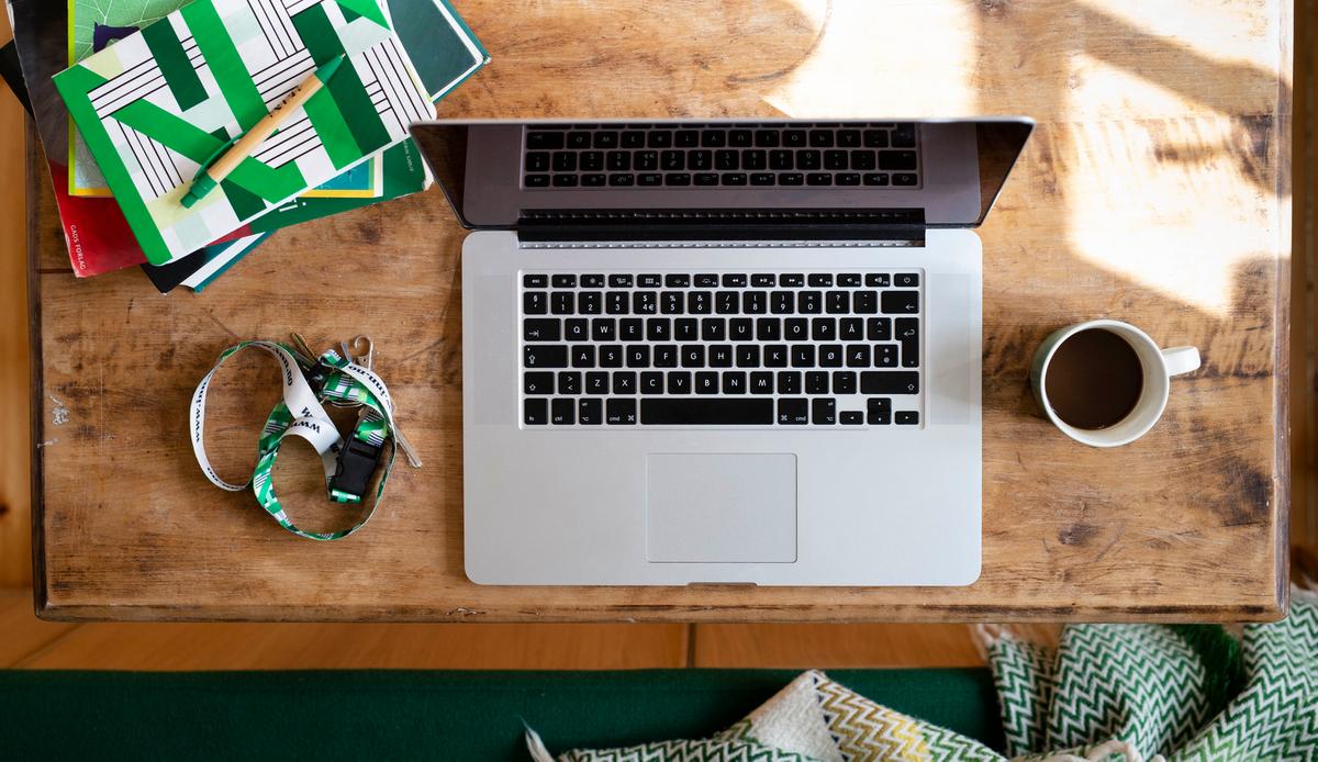 Bilde av laptop, kaffekopp, nøkkelbånd og notatblokk på et trebord