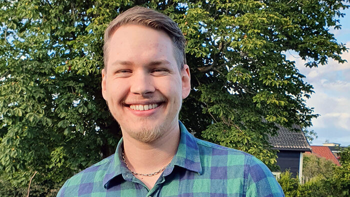Smilende student foran et grønt tre. 