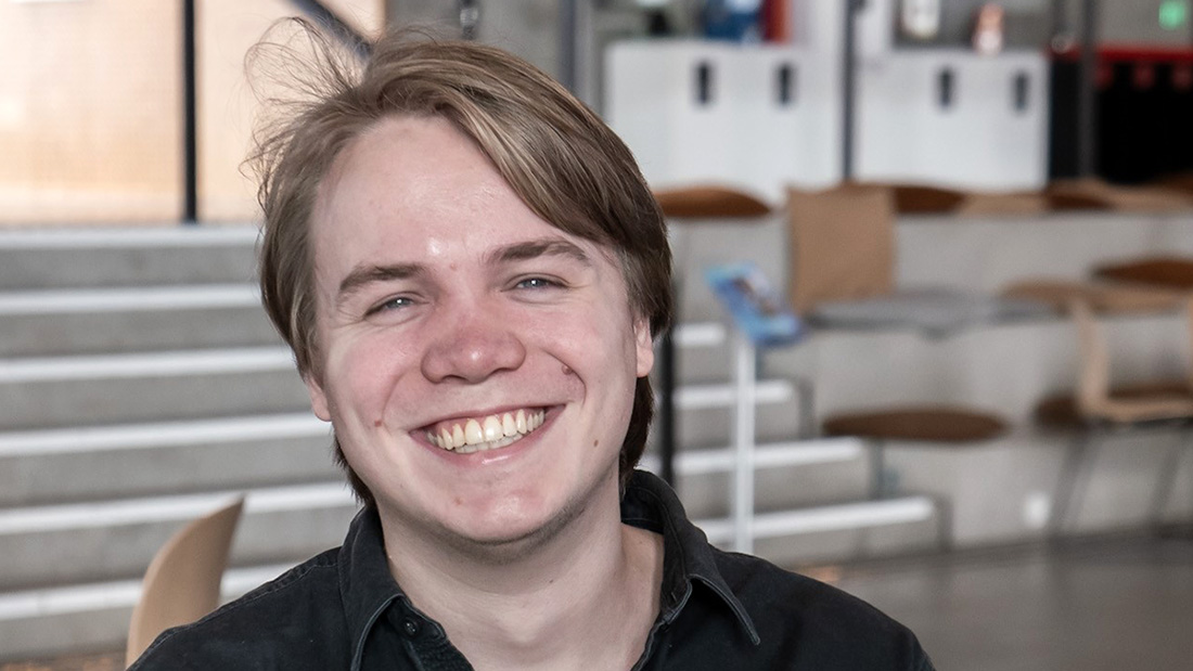 Hvit mann som smiler foran en trapp i bakgrunnen. 