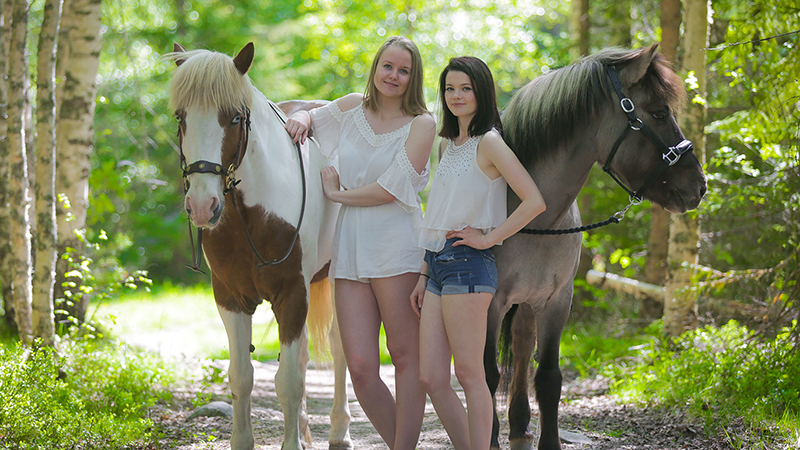To kvinner stående i naturen sammen med to hester. 