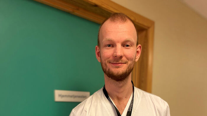 Sykepleiestudent i uniform foran en grønn bakgrunn.