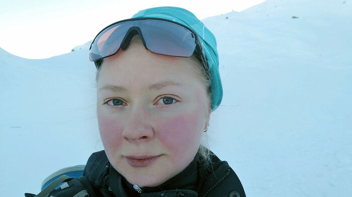 Kvinne med solbriller mot hvit bakgrunn i naturen. 