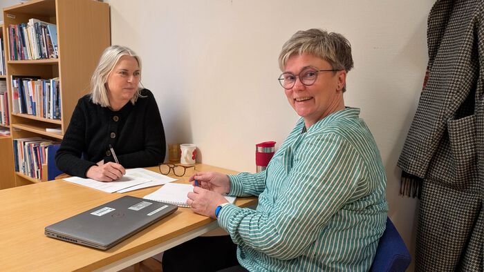Masterstudent og veileder sitter på hver sin side av et møtebord inne på et kontor