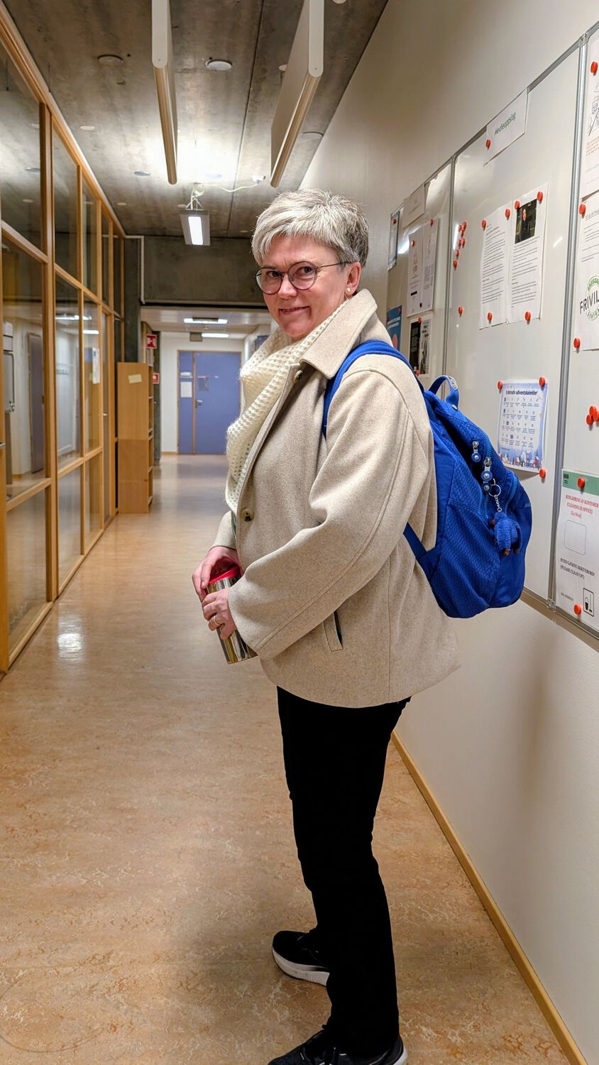 Lise går i korridoren på universitetet med sekk på ryggen og termokopp i hånda, på vei til veiledning