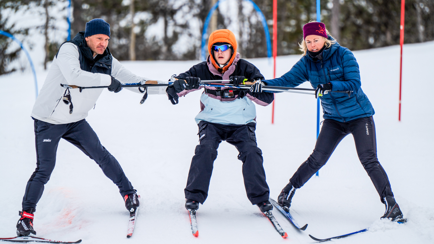 To pesoner holder en tredje person som er blind mellom seg på ski ned en bakke