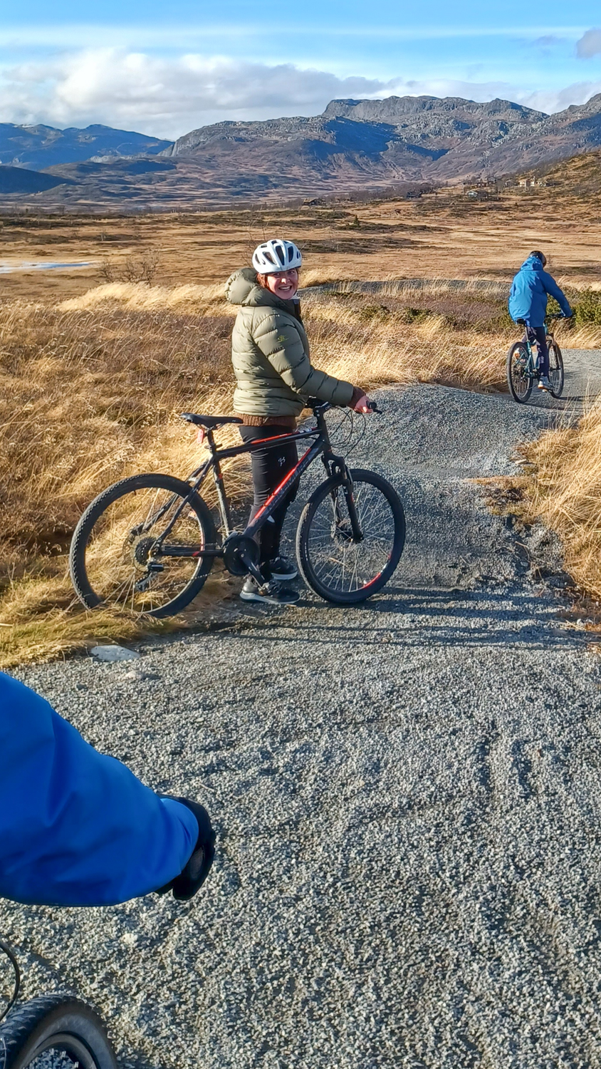 Jente med sykkel på en sti midt i fjellet i høstfarger