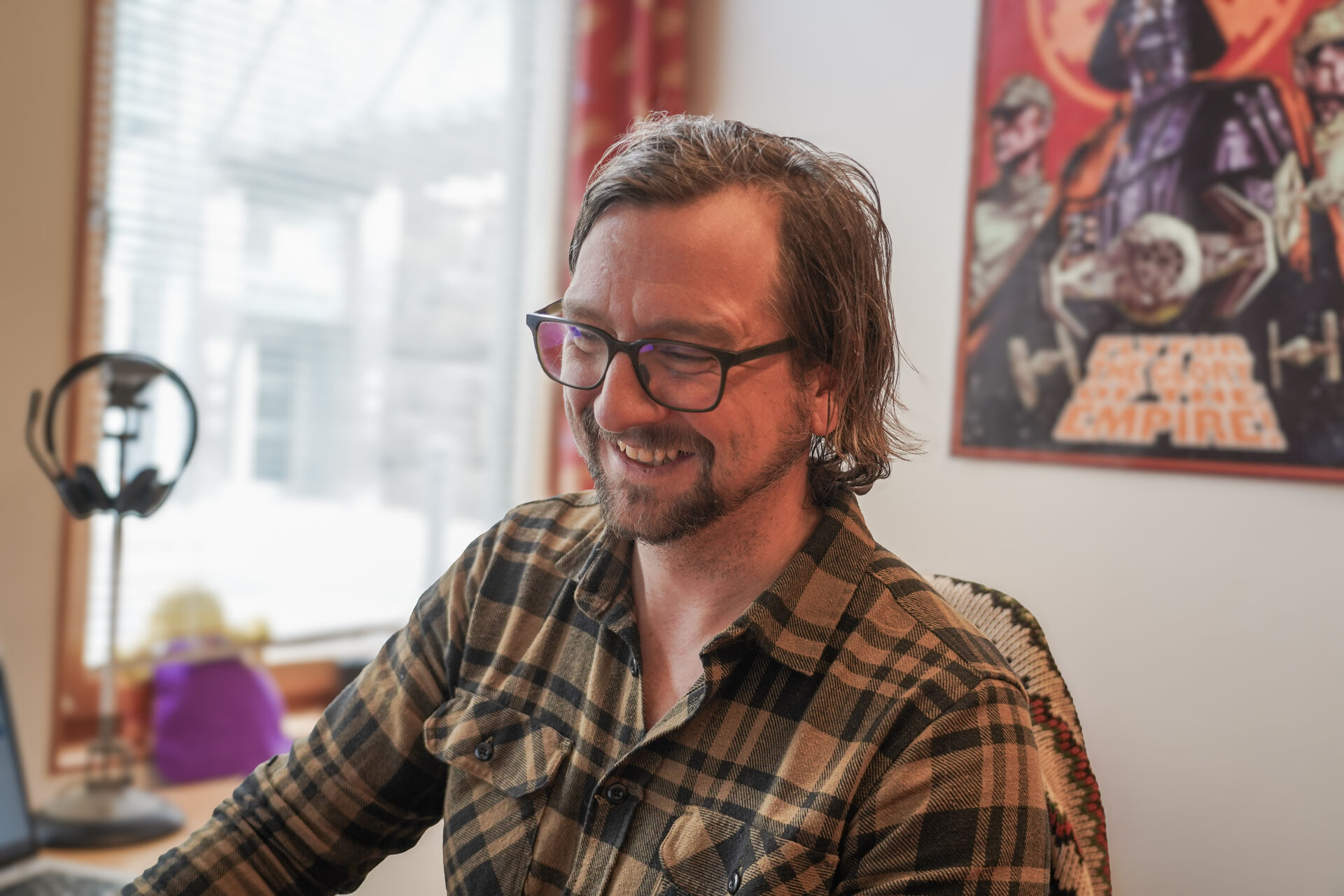 Mann med flanellskjorte sitter foran en PC med en plakat fra Star Wars på veggen i bakgrunnen