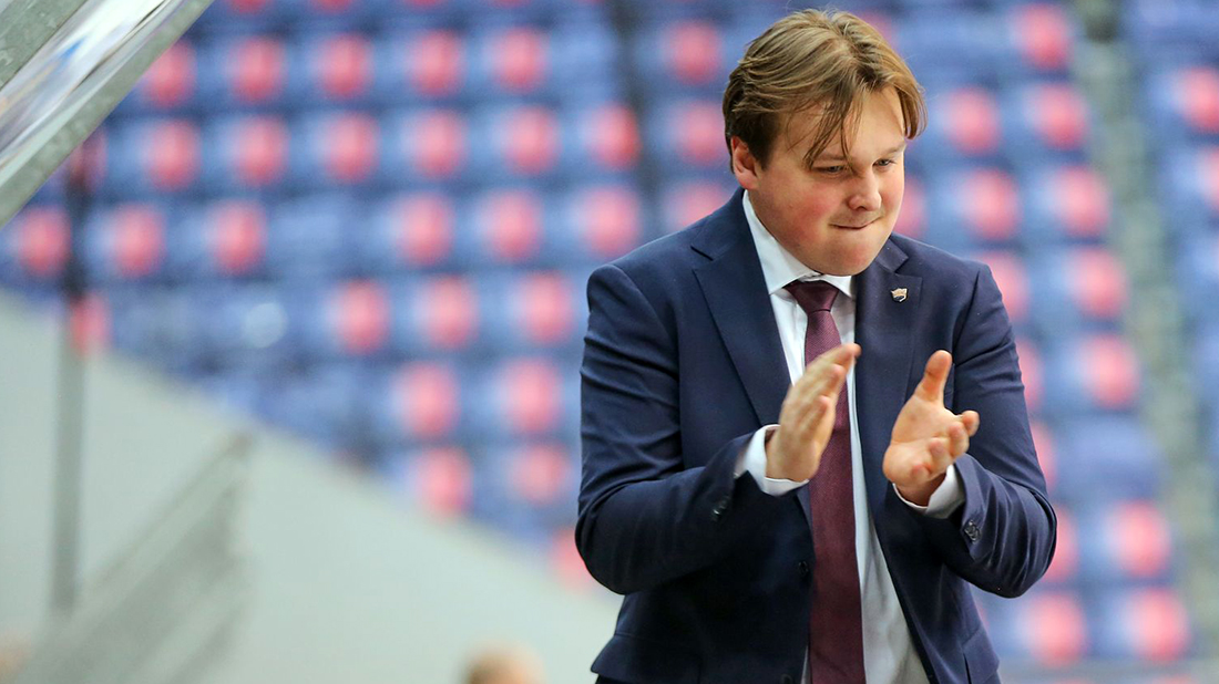 Ishockeytrener Isaac Palmgren iført mørk dress på spillerbenken i Håkons Hall. 