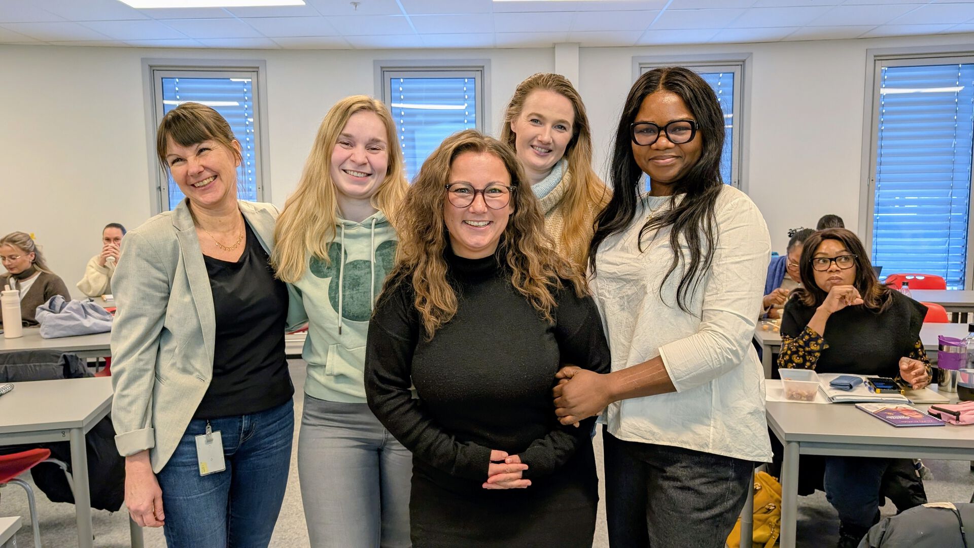 Foreleser og fire studenter i klasserommet. Flere studenter i bakgrunnen