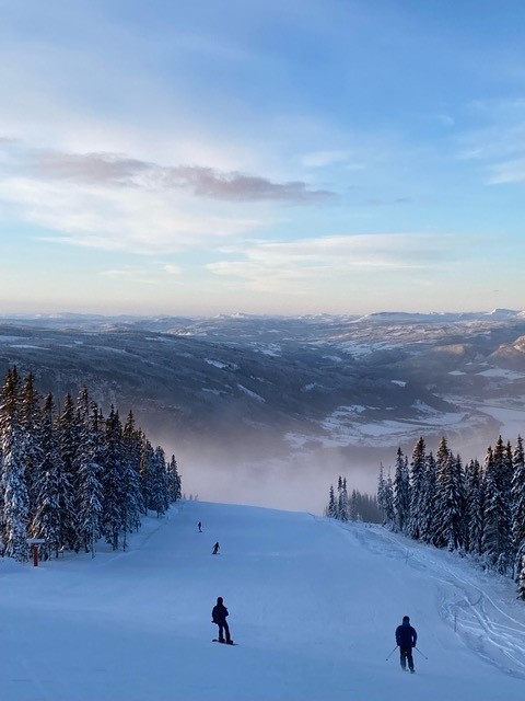 To jenter i en alpinbakke i strålende solskinn og blå himmel. 