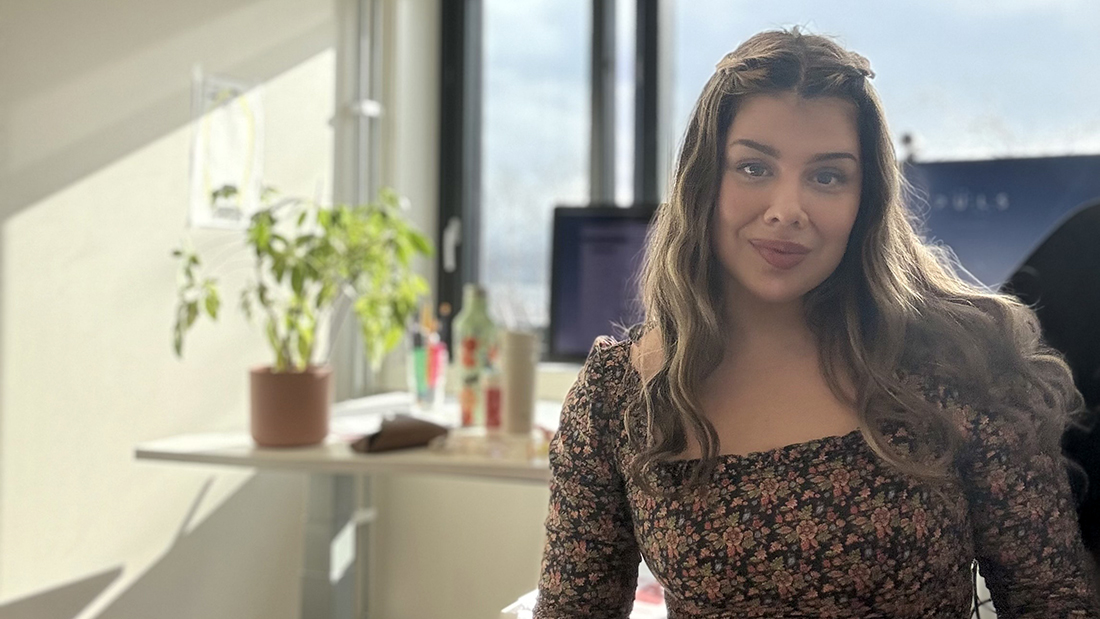 Kvinne som sitter på et lyst kontor med en grønn blomst. 