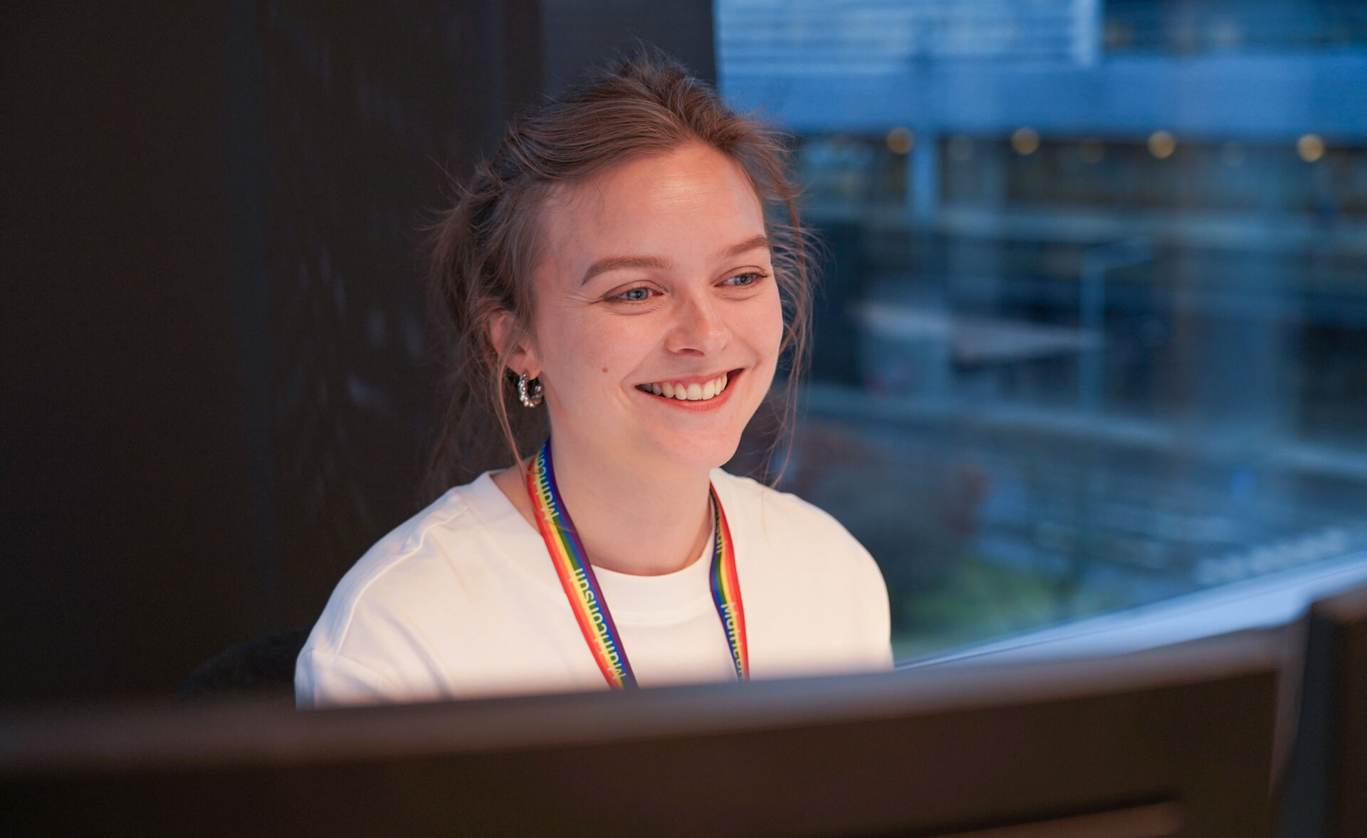 UNg dame med hvit topp smiler og ser på PC-skjermen sin