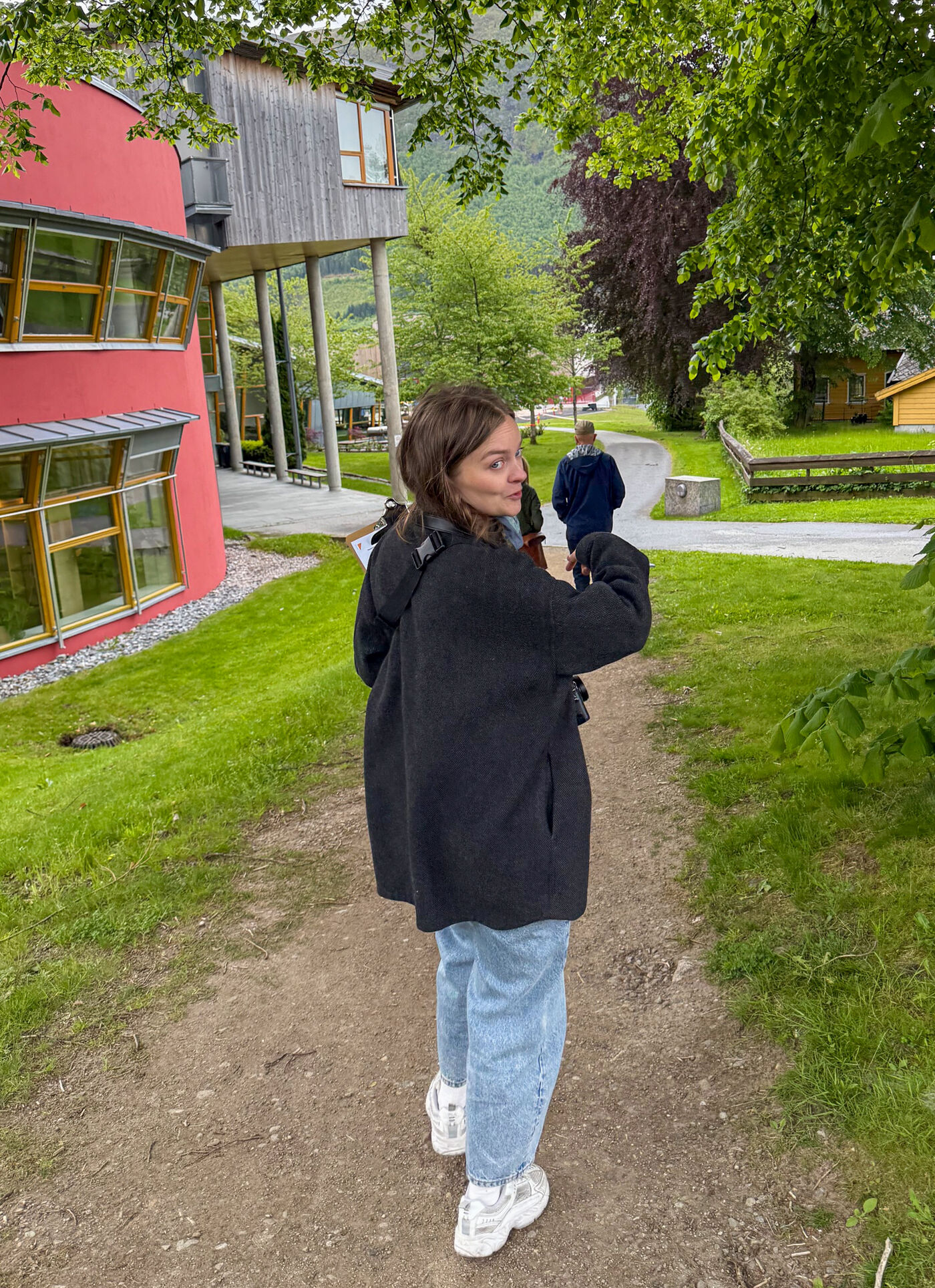 Dame med mørk jakke går på en gressplen med trær og hus i bakgrunnen