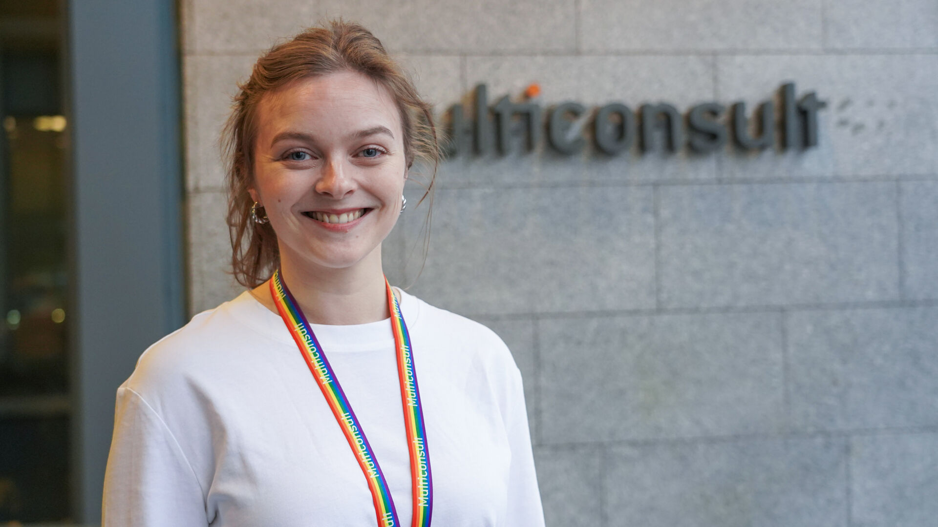 Ung blid dame foran en hvit murvegg med logoen til selskapet Mulitconsult