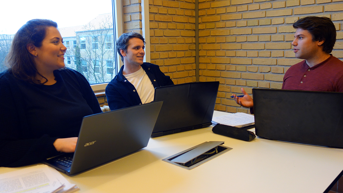 Flere studenter diskuterer rundt et bord. 