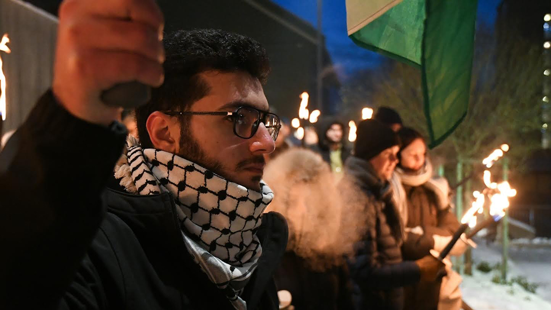 Raed Abuaita kledd i mørke klær mens han holder en fakkel i hånden. 