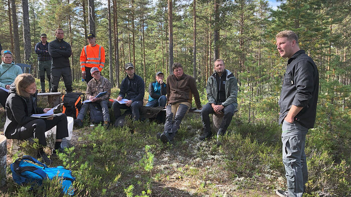 Studenter som sitter ute i skogen mens de lytter til en foreleser. 