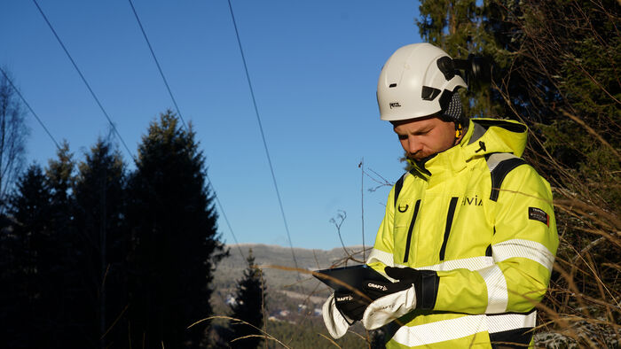 Mann i gul jakke som ser ned på en skjerm ute i skogen. 