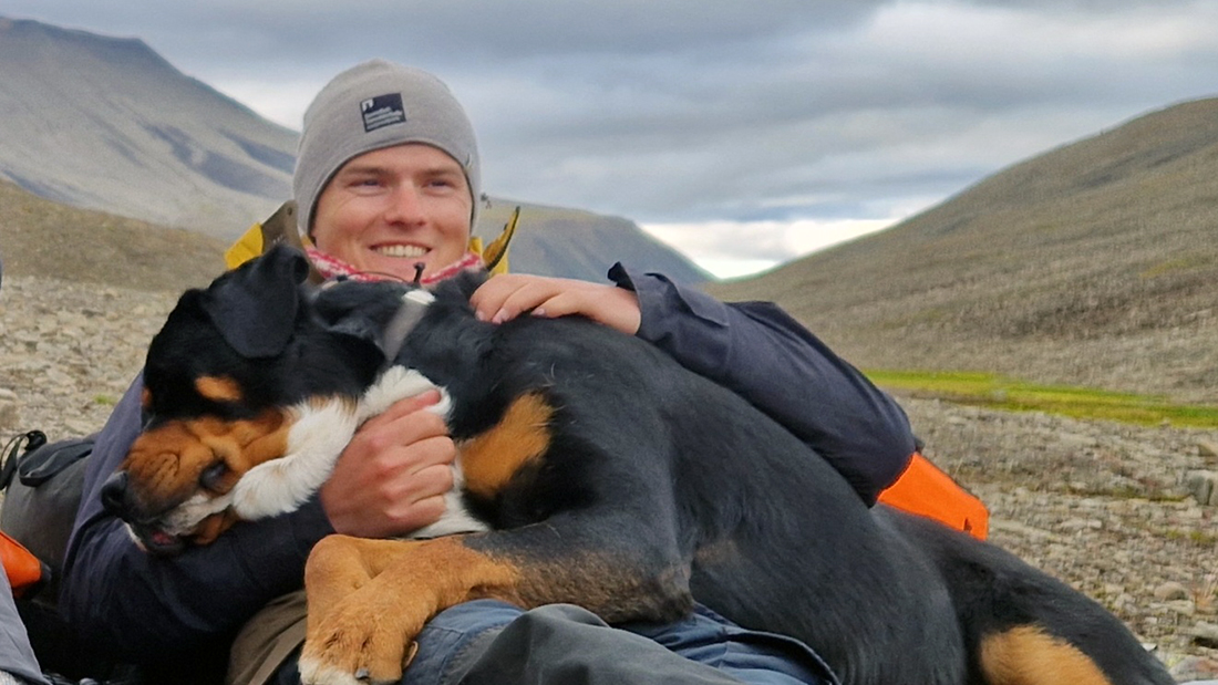 Mann som sitter med en hund ute i naturen. 