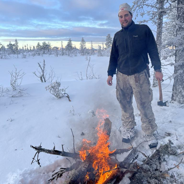 Mann som står ved et bål ute i kulda. 