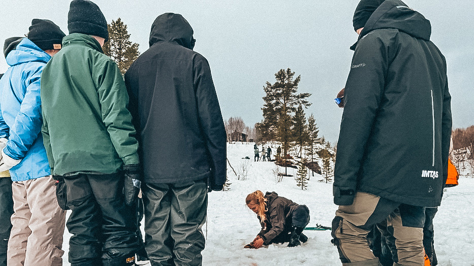 Kvinne som isfisker mens flere personer ser på. 