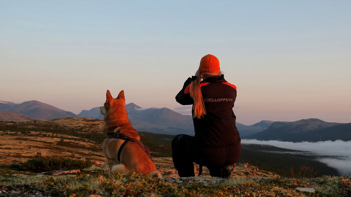 Kvinne som er ute i naturen med en hund ved sin side. 