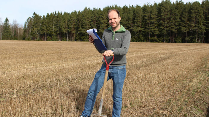 Michael står i feltet og har spade og papir i hånden.