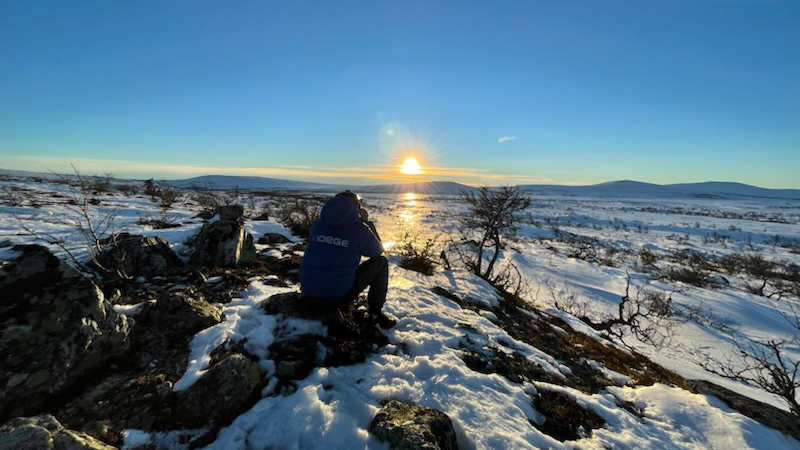 Mann som sitter utendørs og studerer vidda under en helt blå himmel. 