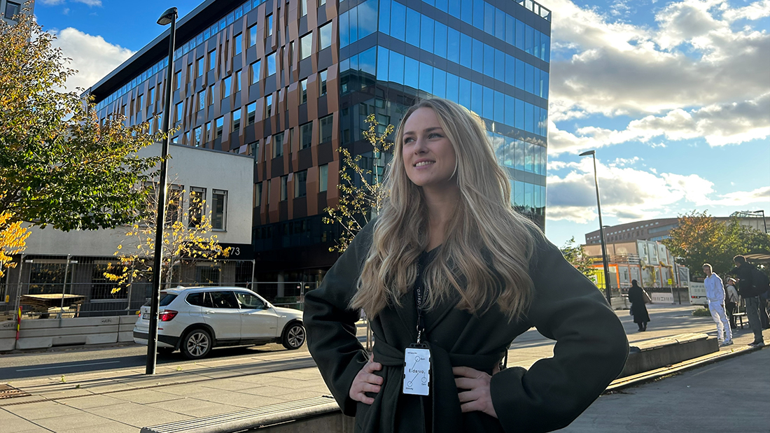 Kvinnelig student i svart kjole utendørs i strålende solskinn. 