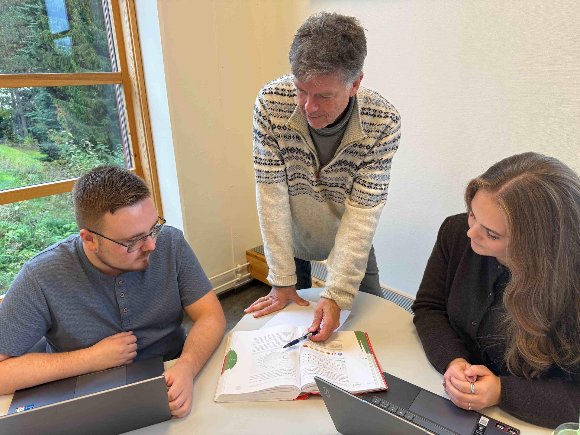 Nora og Nicolay ser i en lærebok sammen med underviser Ole.