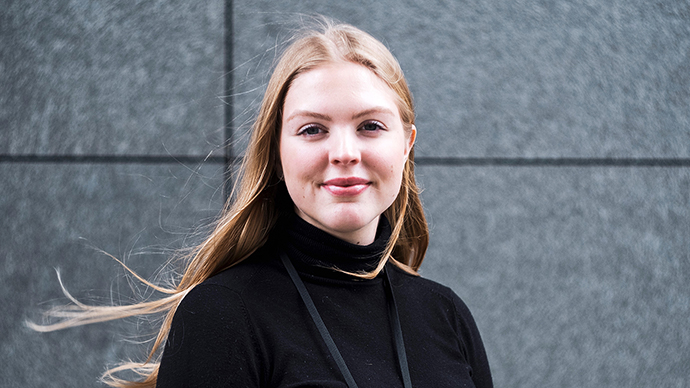 Kvinne kledt i svart foran en mørk vegg. 