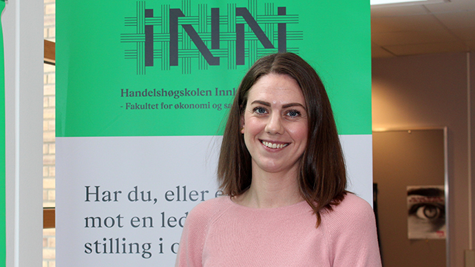 Smilende kvinnelig student foran en messevegg. 