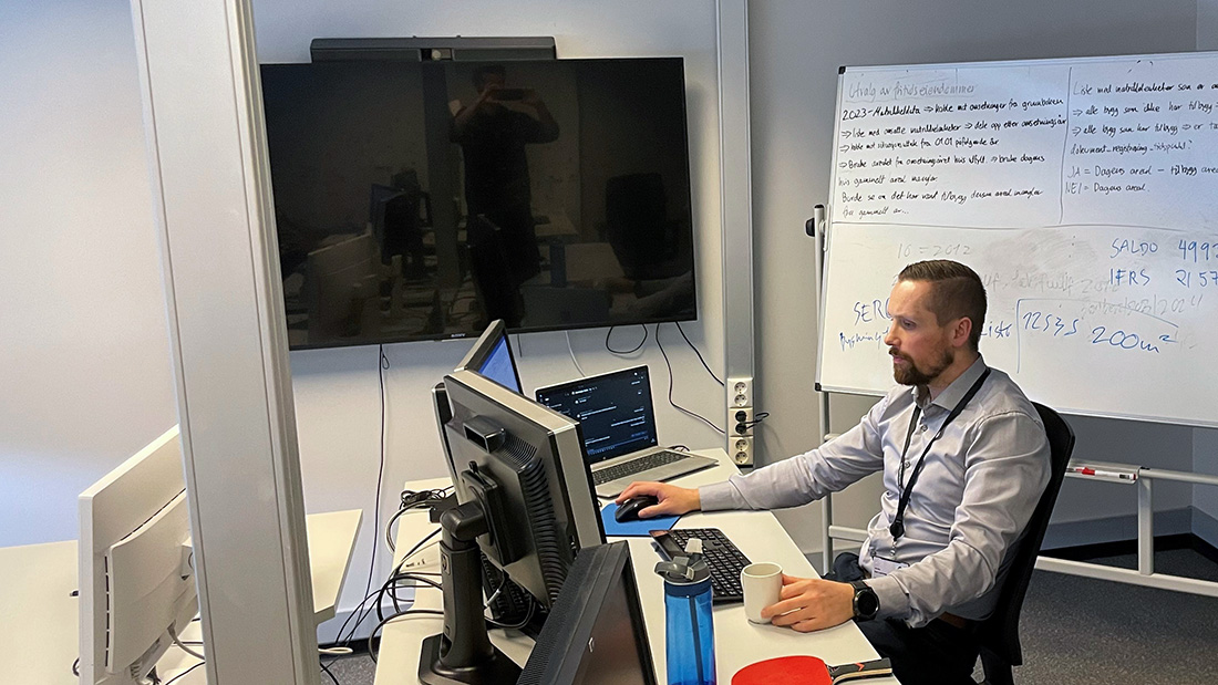 Mann i lys skjorte som sitter i et kontorlokale og jobber. 