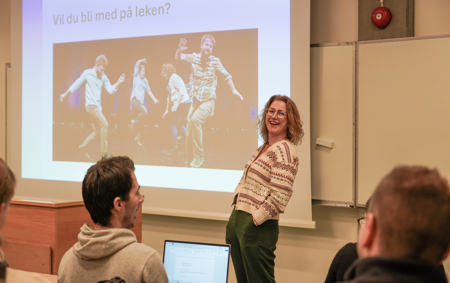 Dame foran en klasse i et auditorium som bøyer seg bakover og ler
