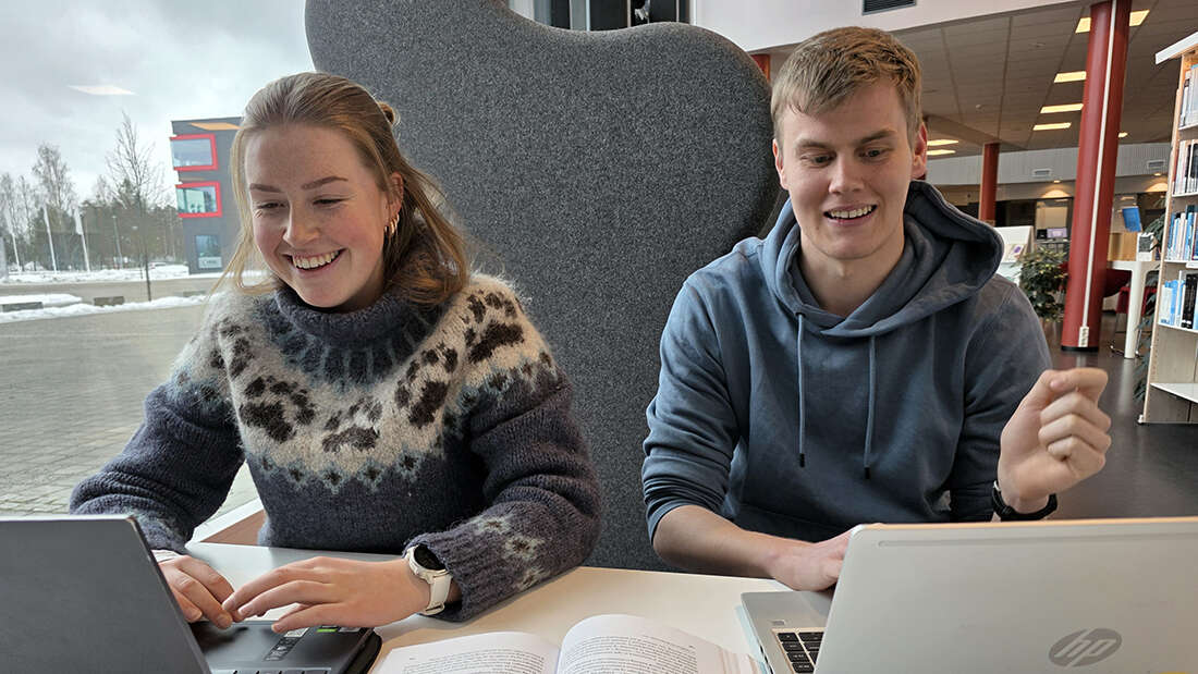 To smilende studenter på et bibliotek.