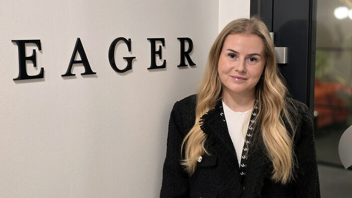Kvinne med lyst hår i mørke klær foran en mørk vegg. 