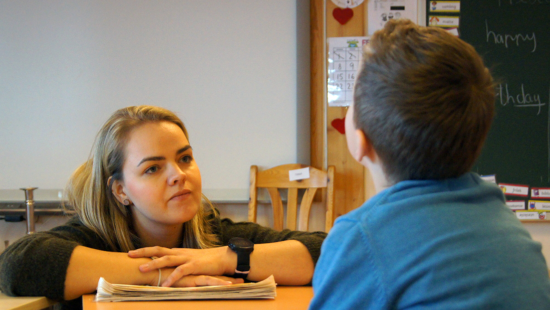 Lærer Svanhild Barlund hjelper en elev ved pulten hans.