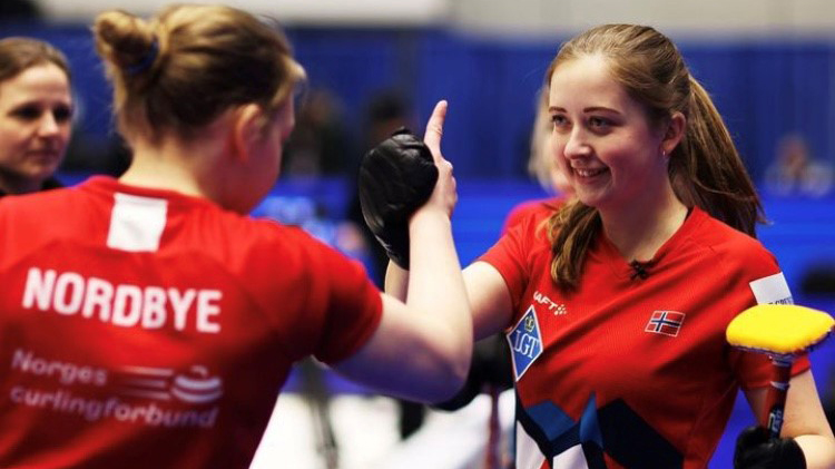 To kvinnelige curlingspillere i røde t-skjorter som utveksler blikk og håndhilser på hverandre. 