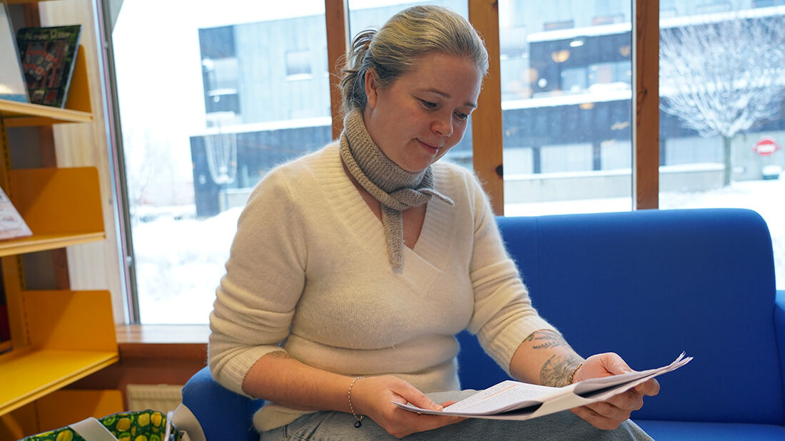 Kvinne i hvit genser som sitter i en sofa mens hun leser et dokument. 