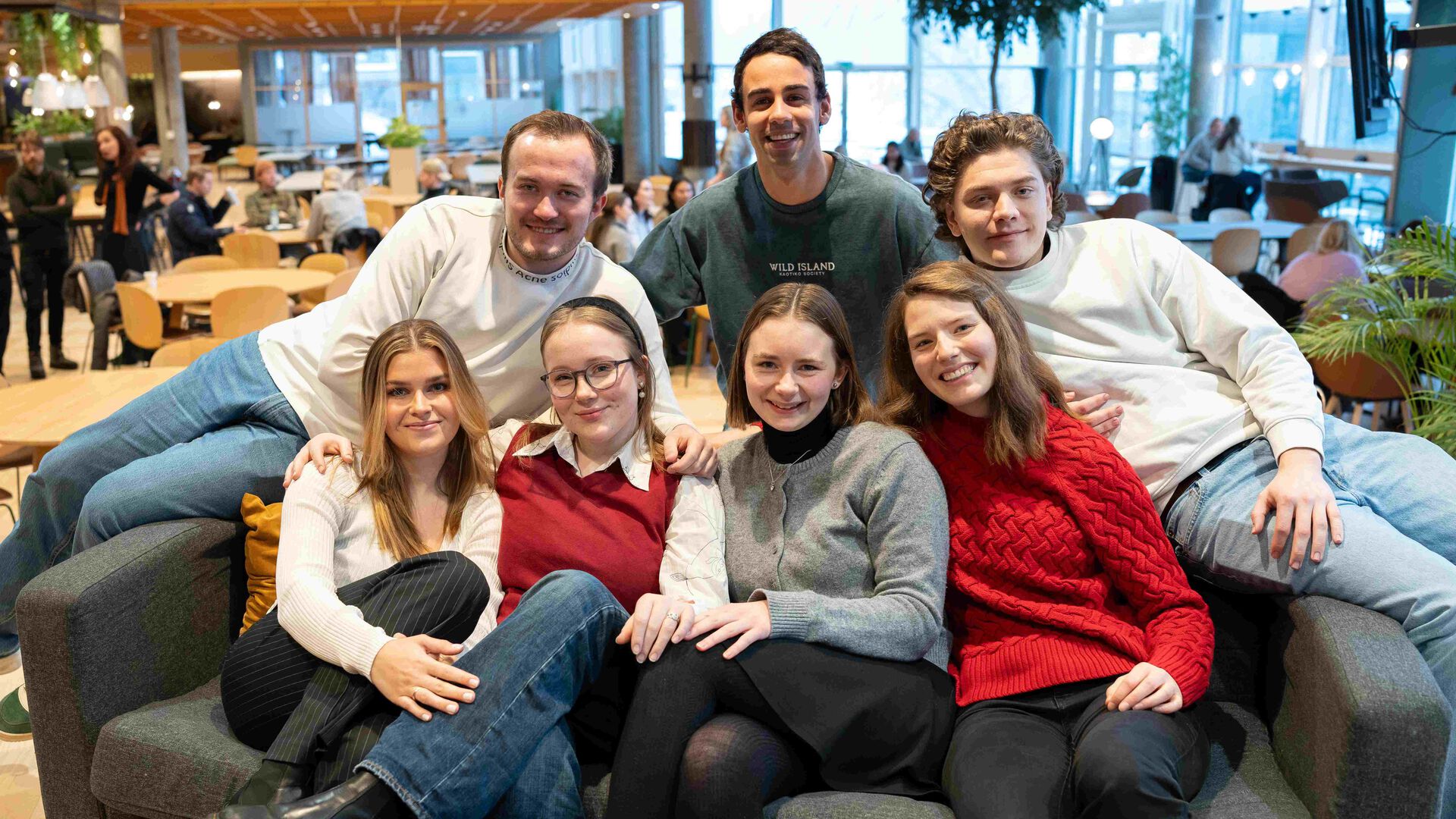 Sju studenter samlet i og oppå en sofa i kantina i Lillehammer, alle ser smilende i kamera.