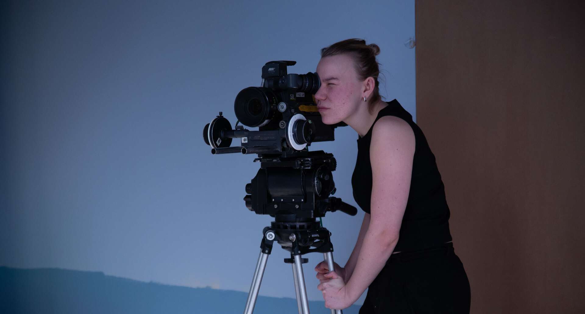 Fotograf med fiilmkamera i studio med blå bakgrunn.