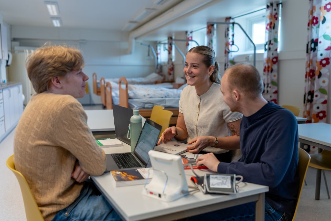 Vernepleiestudenter som sitter rundt et bord inne i en øvingssal. Øvingssalen har patientsenger.