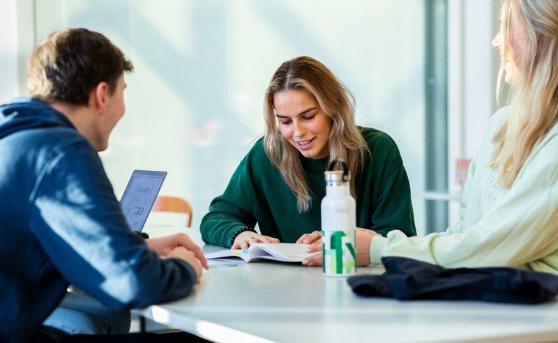 Studenter samlet rundt et bord som smiler og ler, en av de har en høgskole flaske i hånden.