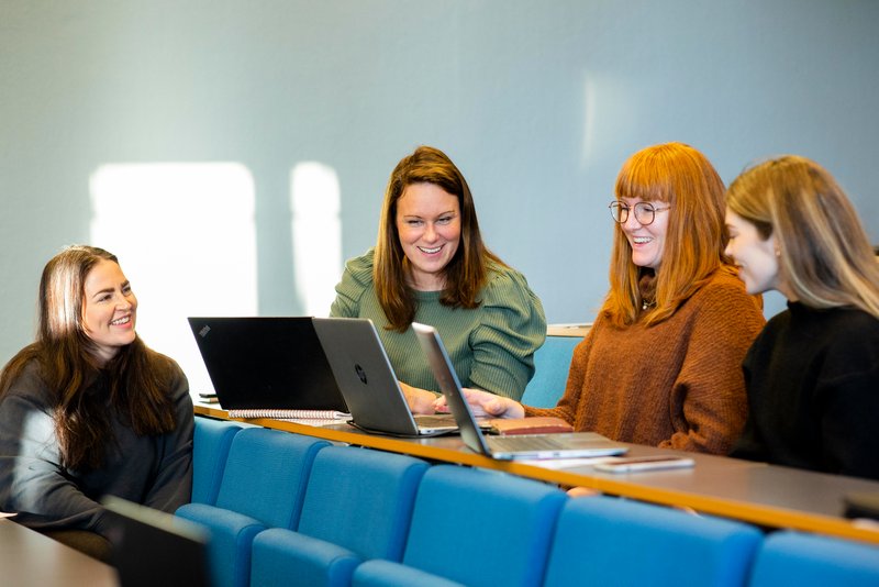Studenter i forelesningssal som sitter med laptops fremfor seg og samhandler om noe på den ene av skjermene.