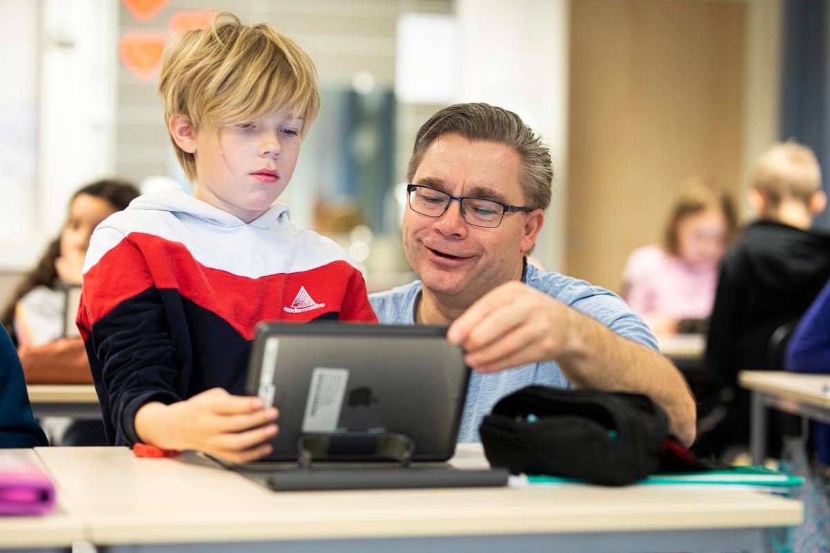 En elev ser på ipad sammen med en mannliglærer ved en skolebenk i klasserommet.