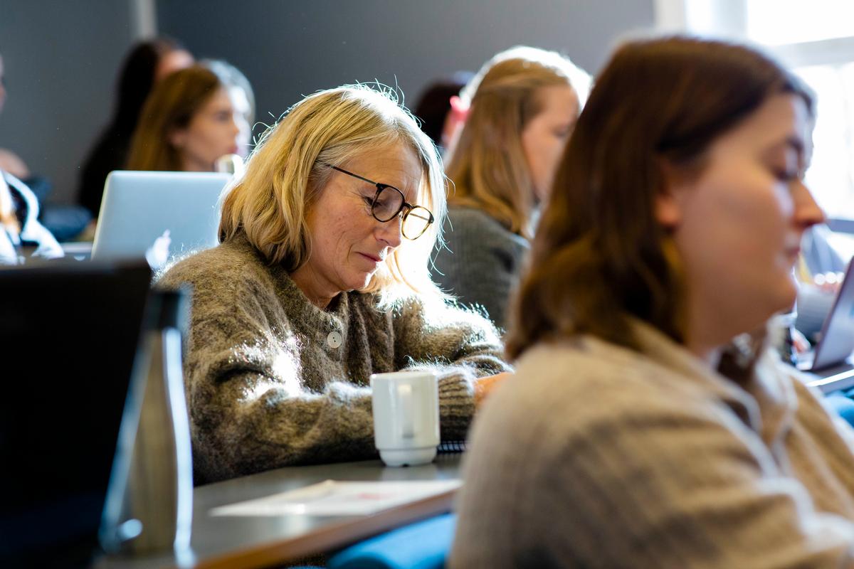 Middelaldrende dame som sitter i forelesning og ser ned på notater